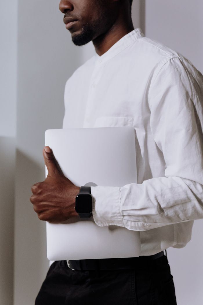 A professional adult man in a white shirt holding a laptop indoors, showcasing modern technology and business style.